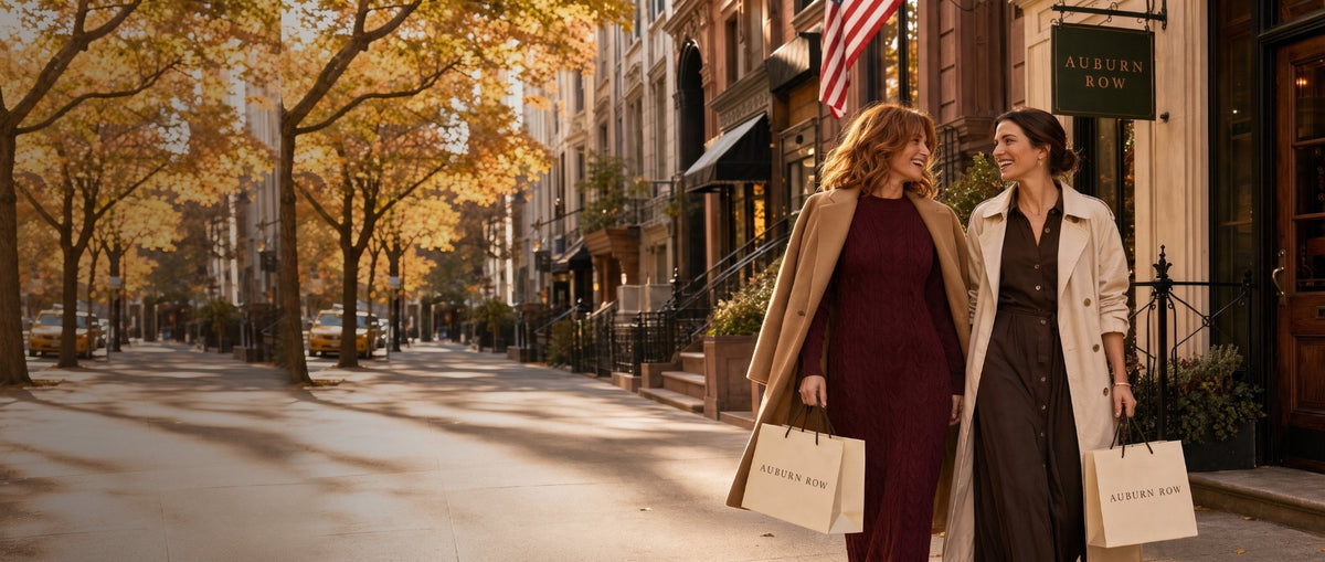 Two women walking a tree-lined New York brownstone street in autumn with Auburn Row shopping bags, past the Auburn Row boutique sign